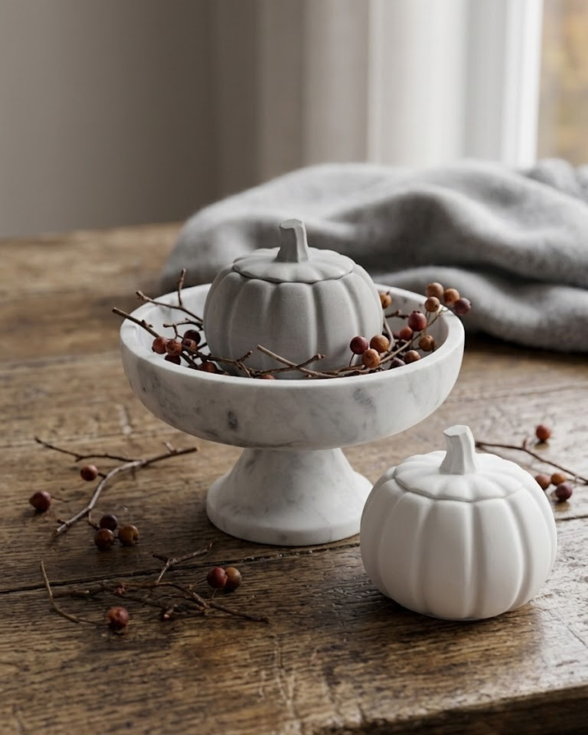 White ceramic pumpkin-shaped candle jar with lit wick on a gray base tray