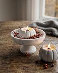 Gray ceramic pumpkin-shaped candle jar with lit wick and small decor berries