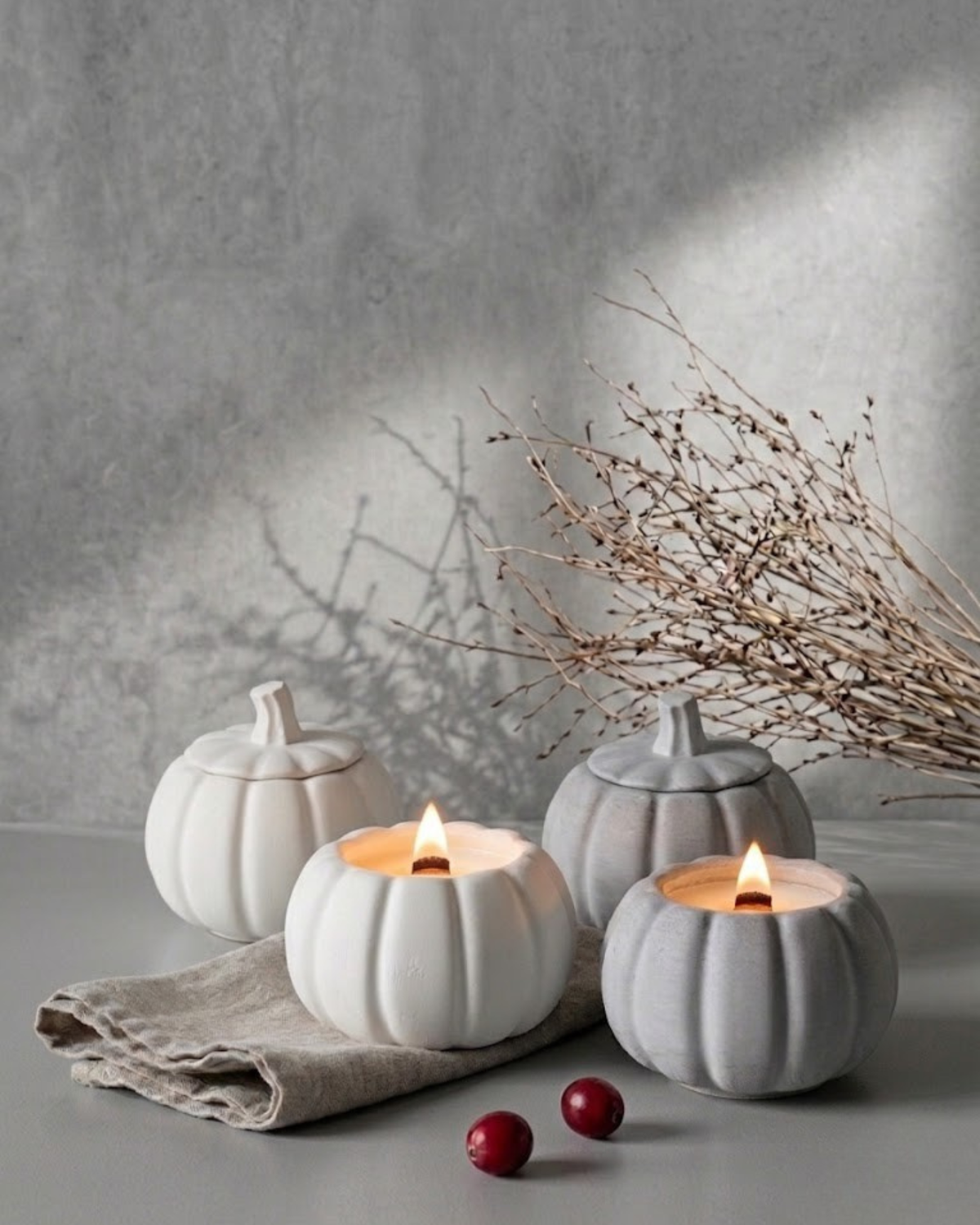 Set of white and gray ceramic pumpkin-shaped candle jars with lit flames