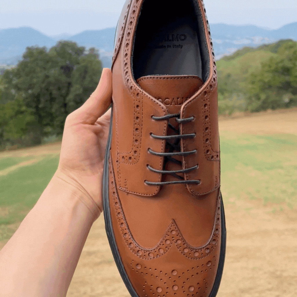 Cognac lace-up wingtip oxford shoe held in hand, showing brogue details