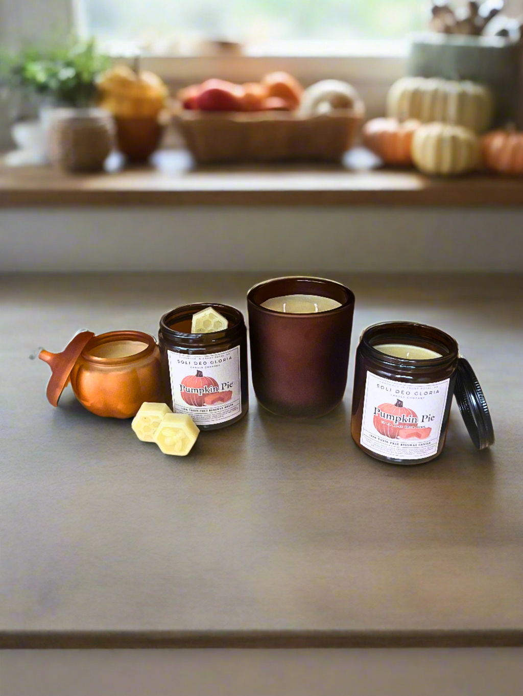 Three beeswax candles in brown glass jars with honeycomb wax pieces and small scoop.