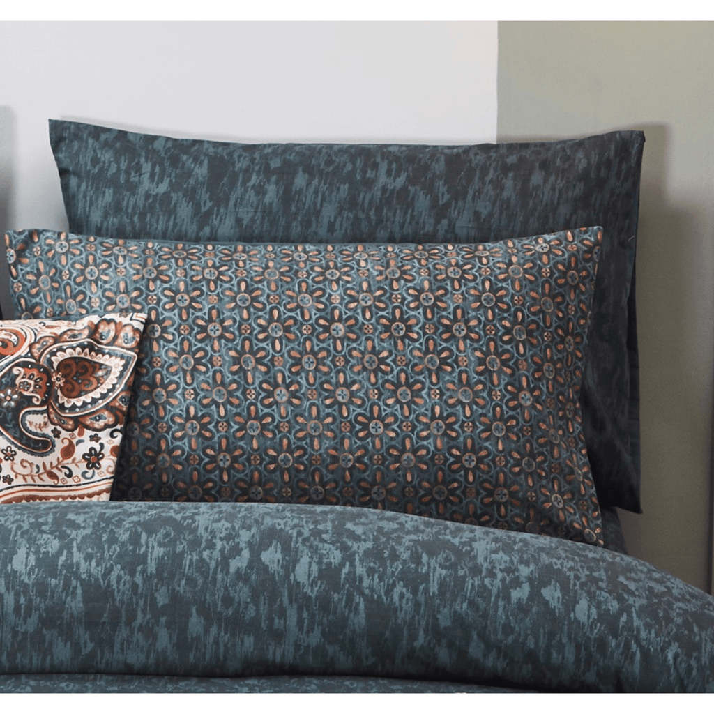Dark teal pillowcase with lattice floral watercolor motif, shown on a bed