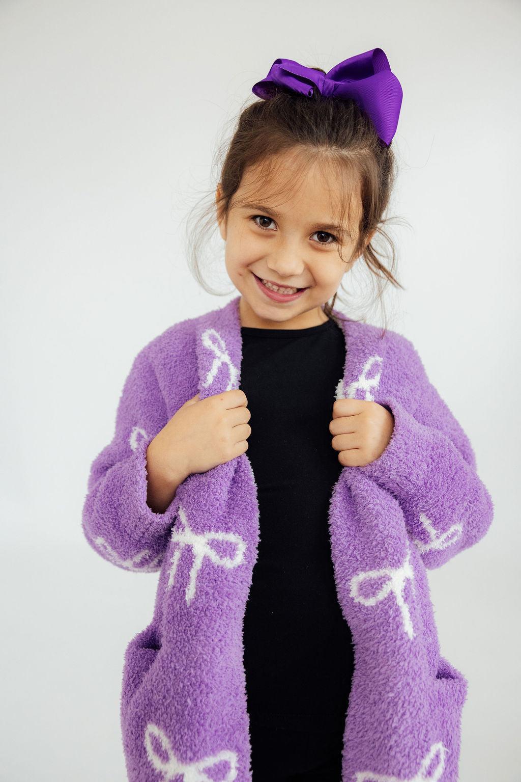 Girls purple fuzzy cardigan with bow print, open front over dark shirt.