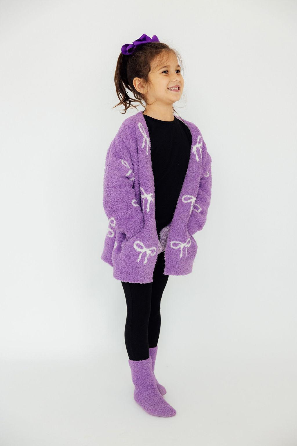 Girls purple bow-print cardigan with long sleeves, open front, worn with leggings.