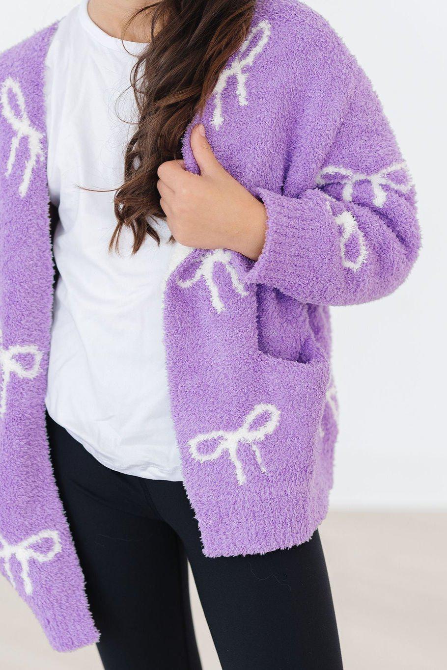 Purple fuzzy cardigan with bow print, open front, close-up of front pocket area.