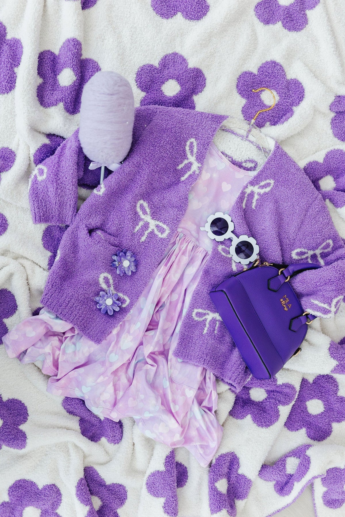 Purple bow-print cardigan sleeve and front pocket detail, laid out flat.