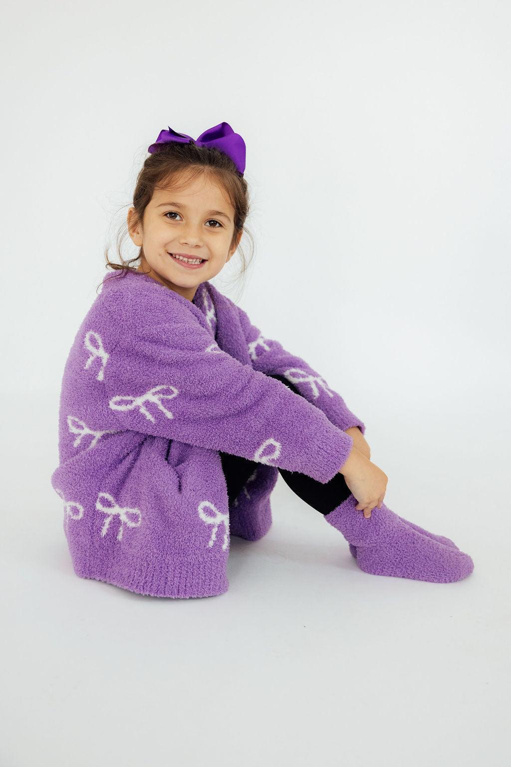 Purple plush cardigan for girls with bow pattern, open front and long sleeves.