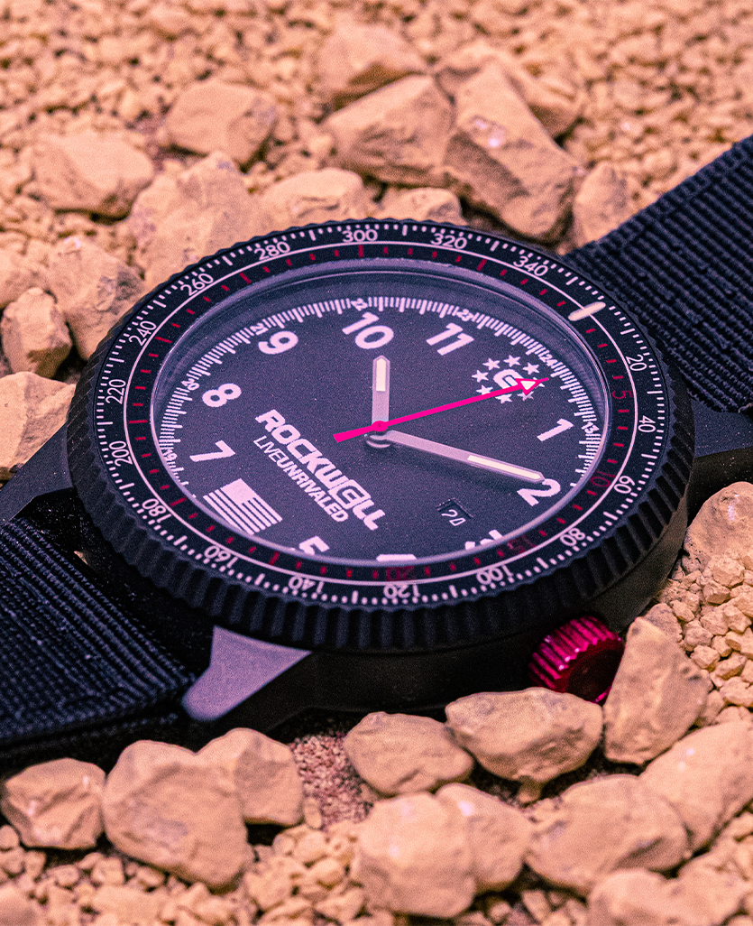 Vanguard black watch with black dial, pink bezel markings, and analog hands