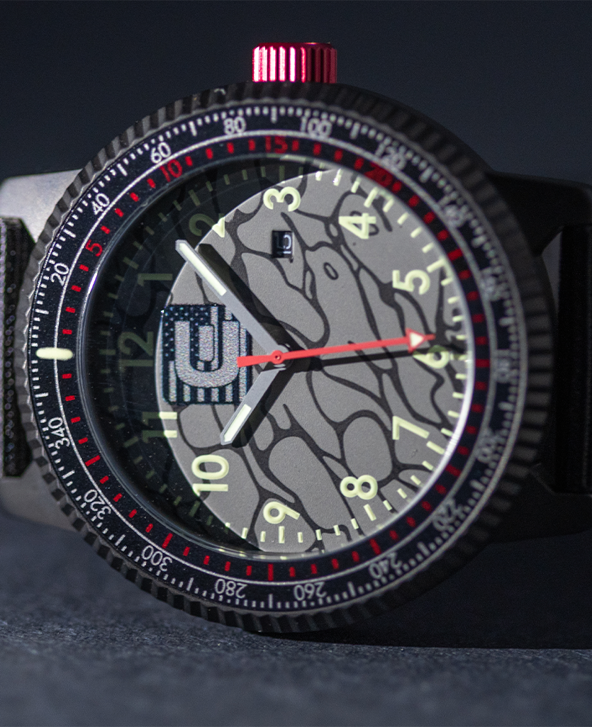 Camo dial wristwatch with black case, red minute markers, and black fabric strap