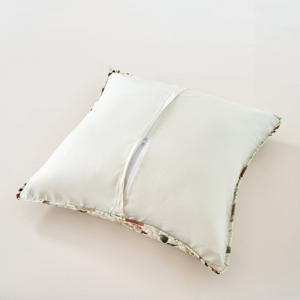 Cream throw pillow with floral border and green-beige botanical piping along the edges.