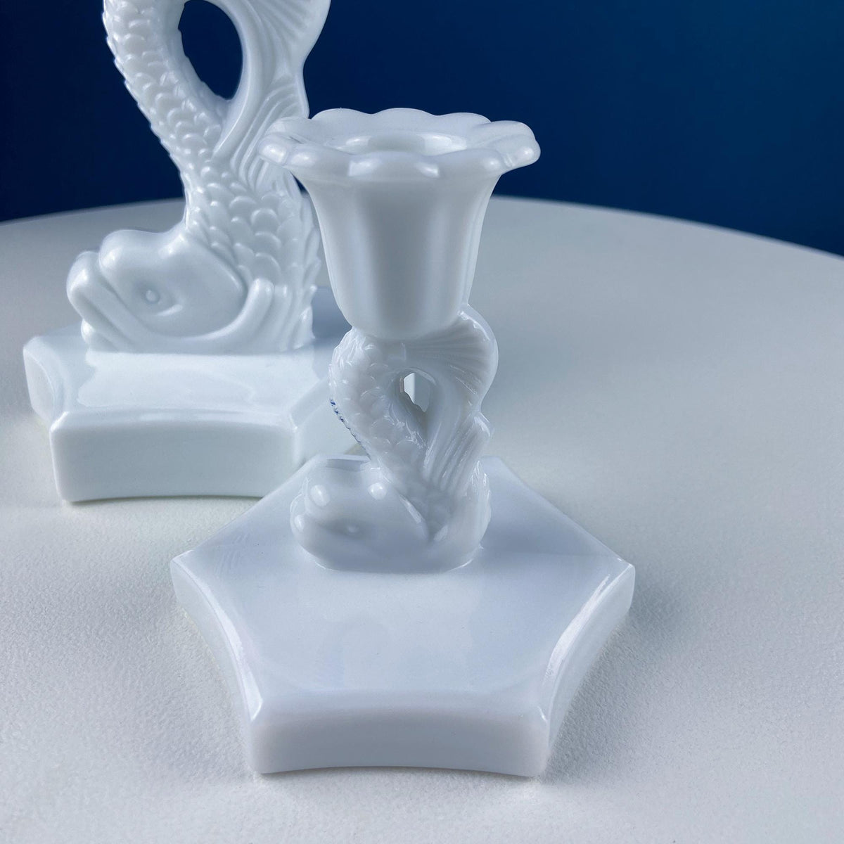 White milk glass dolphin candle holder with curved candle cup and ornate base