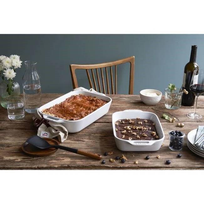 Two white ceramic baking dishes with handles, one filled with baked food