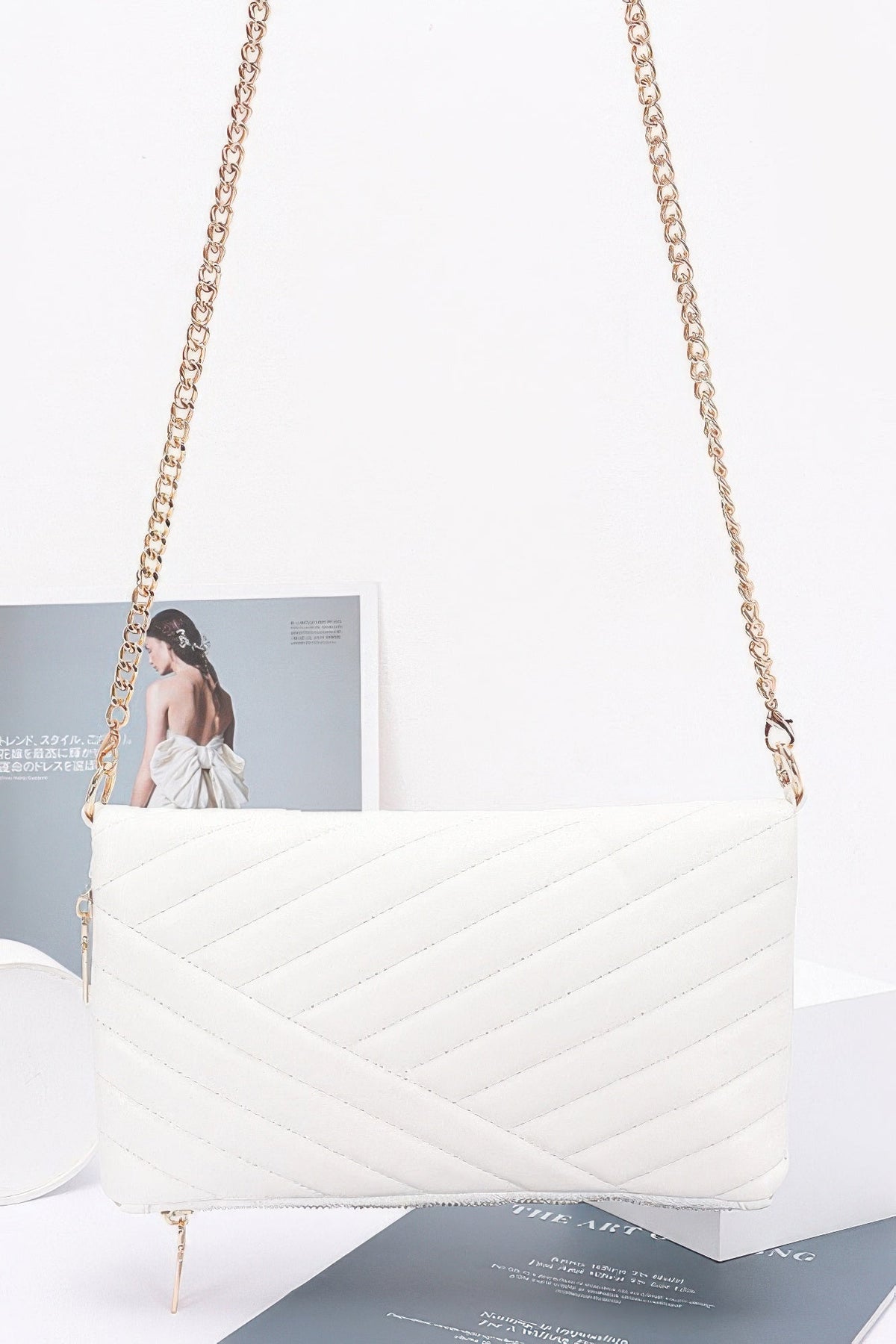 White quilted clutch with long chain strap and gold-tone zipper, diamond chevron pattern