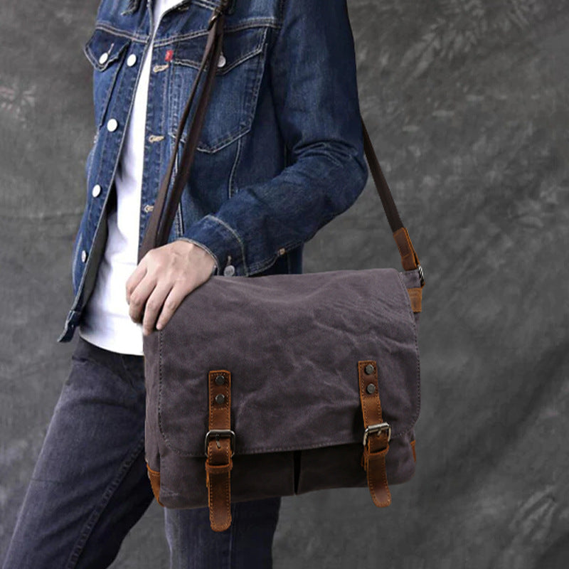 Waxed canvas crossbody messenger bag, dark gray with leather buckle straps and flap front.