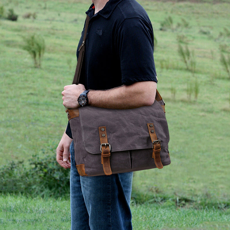 Waxed canvas crossbody bag on person, dark gray front flap with leather buckle tabs.