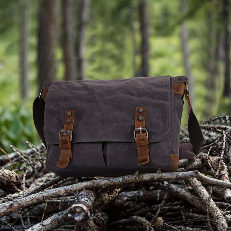 Waxed canvas messenger bag, dark gray with two front leather buckle straps and side handles.