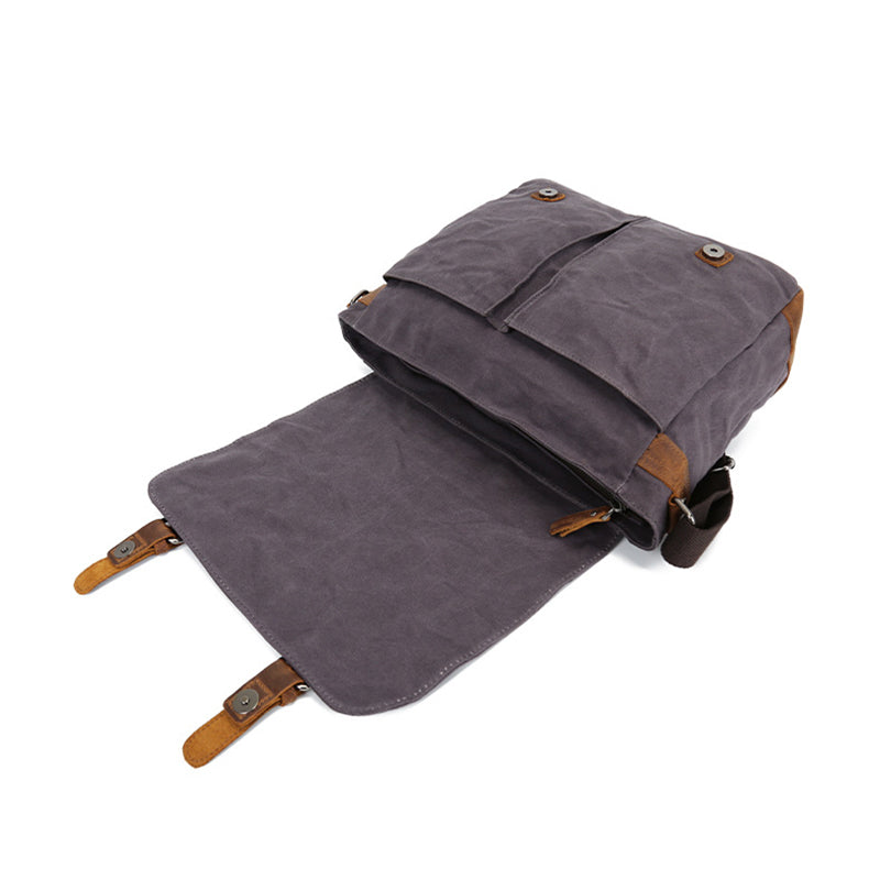 Rolled waxed canvas crossbody bag folded out flat view, dark gray with leather details.