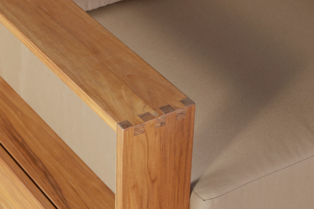 Teak wood armchair corner detail with visible grain and beige cushion beside it.