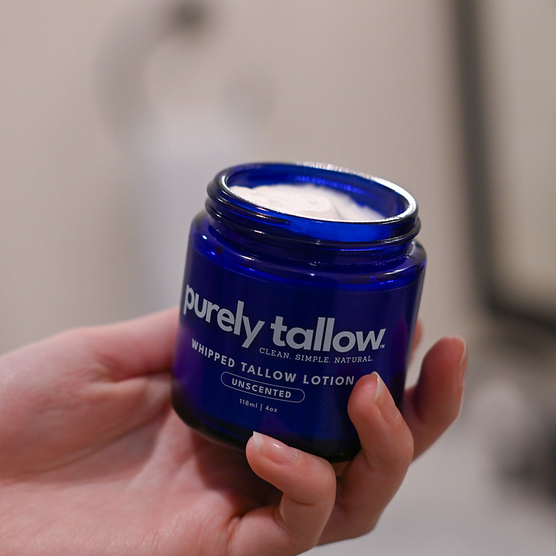 Whipped tallow lotion jar held in hand, blue label and open lid