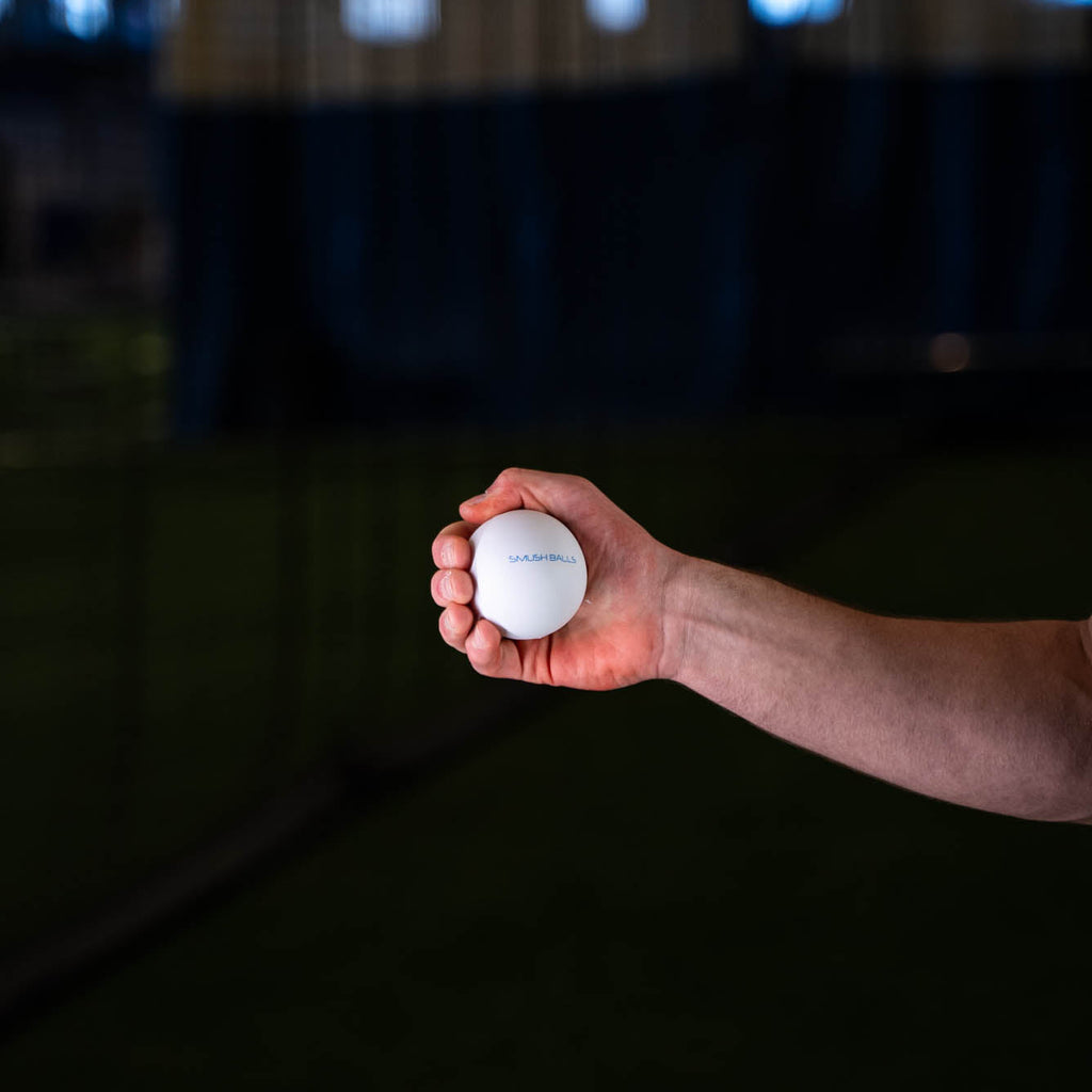 Hand holding a white SMUSH BALLS stress ball with SMUSH BALLS logo.