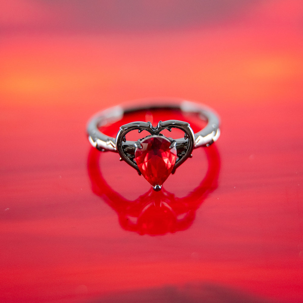 Silver ring with red teardrop gemstone and black accent settings