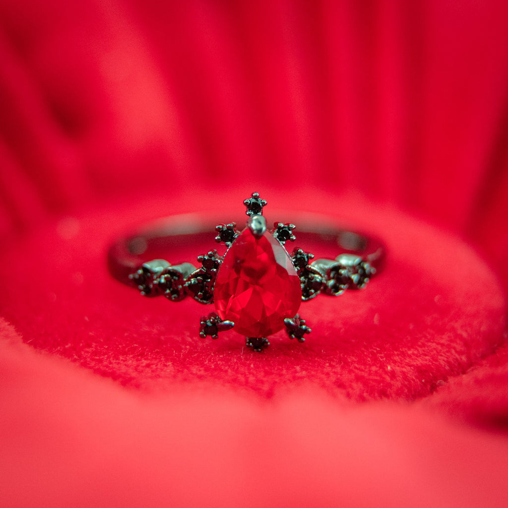 Silver ring with red teardrop gemstone, surrounded by green floral accents