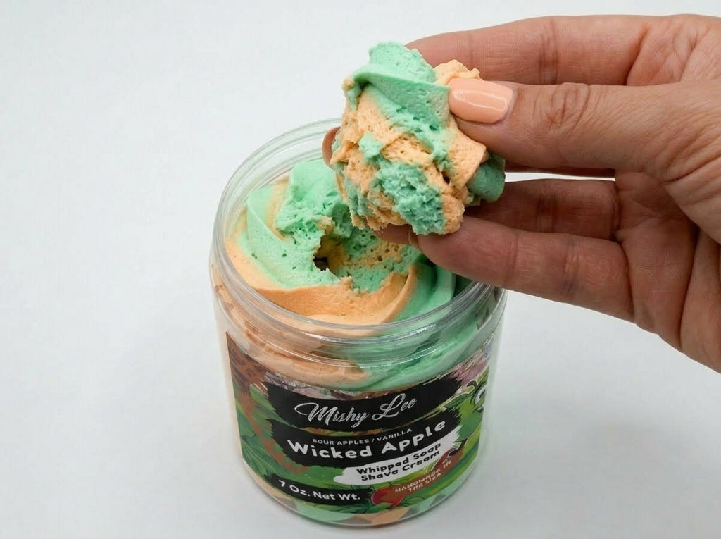 Hand holding a scoop of whipped soap and shave cream in green and orange layers.