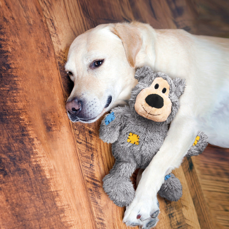 Gray plush bear dog toy with yellow knot rope details, held by a white dog