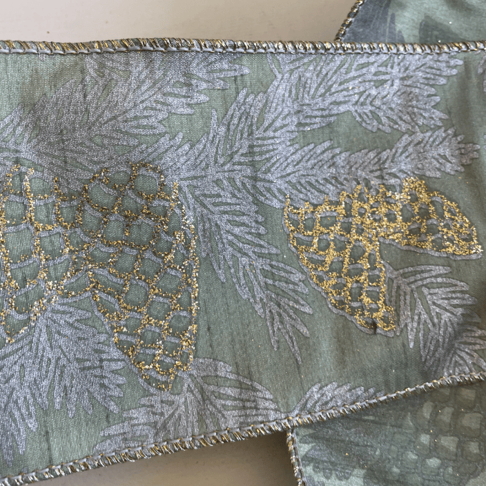 Close-up wired ribbon fabric in green with gold and silver pinecone and leaf embroidery