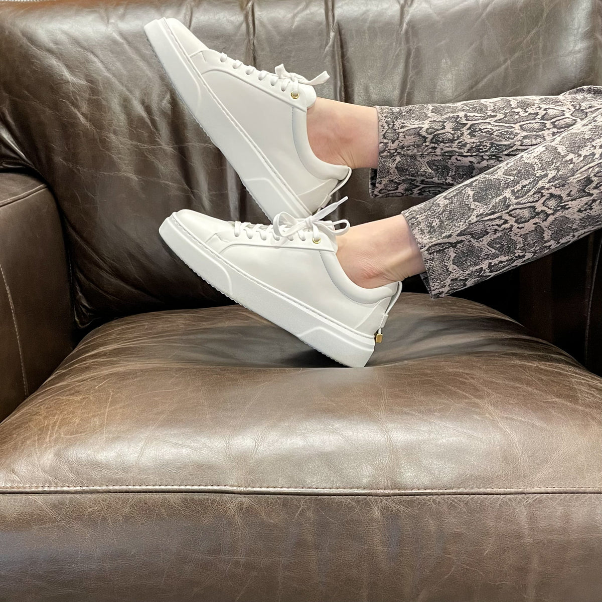 White low-top sneakers sitting pose on couch with thick sole and gold accents