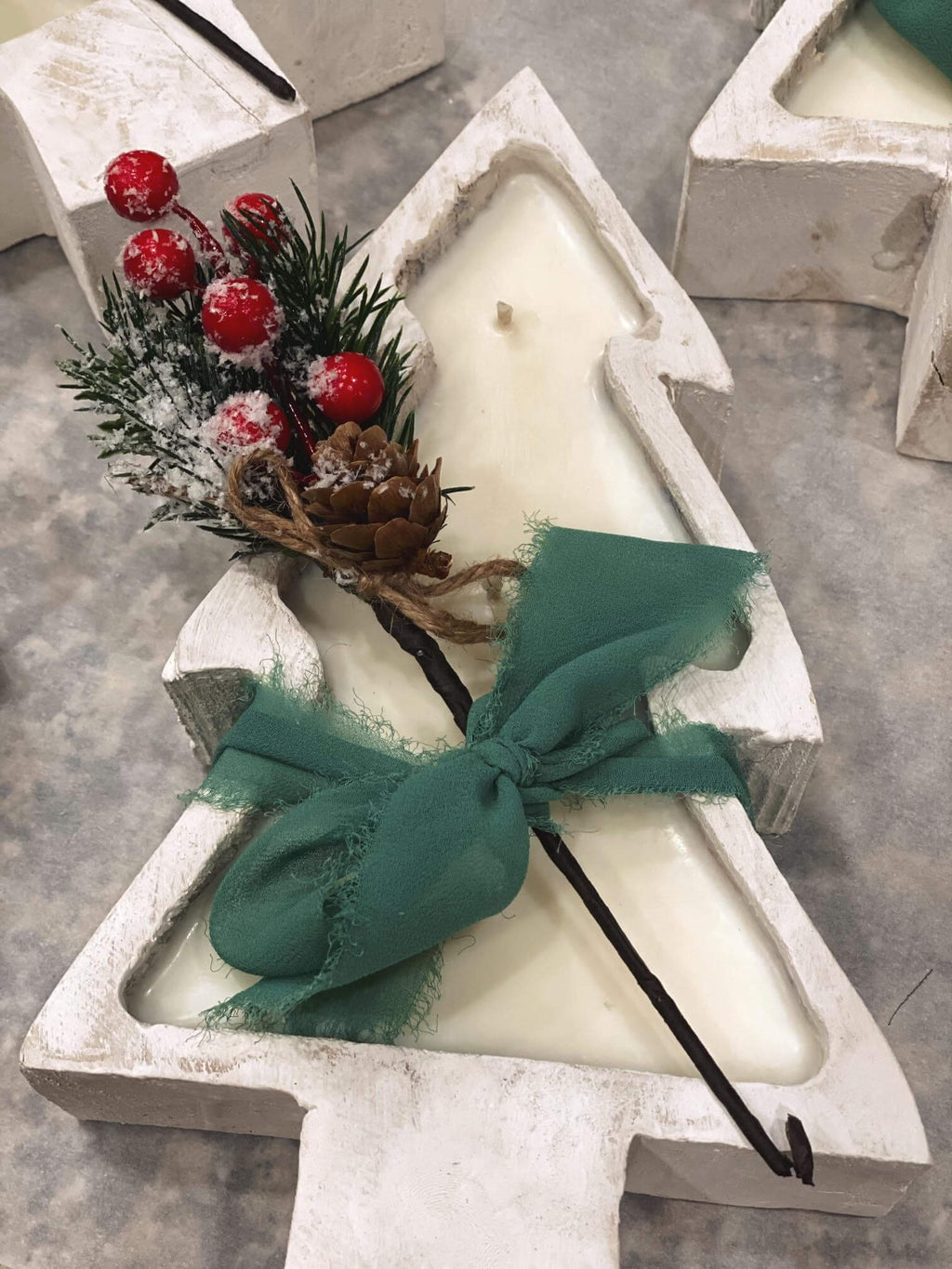 Sculptural Christmas tree candle in white with green ribbon bow, pinecone, and red berries
