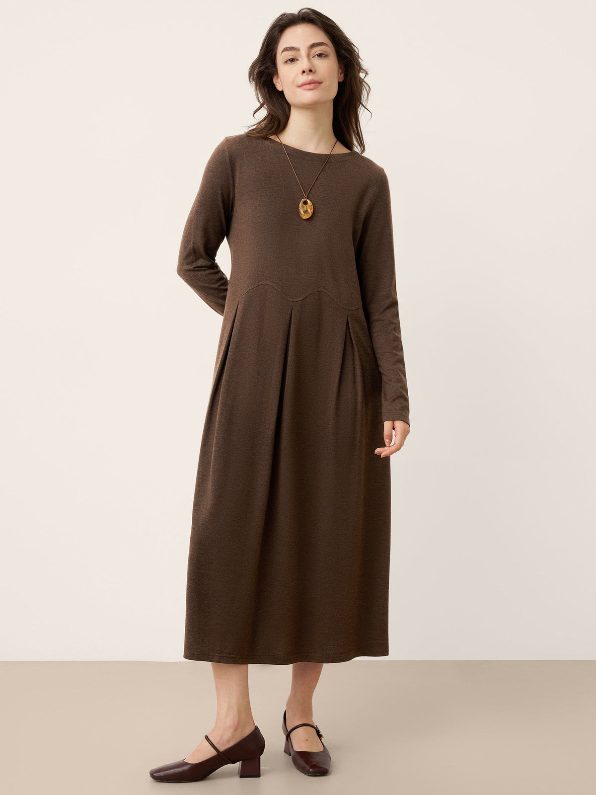 Brown wool midi dress with long sleeves, rounded neckline, and curved pleat shaping.