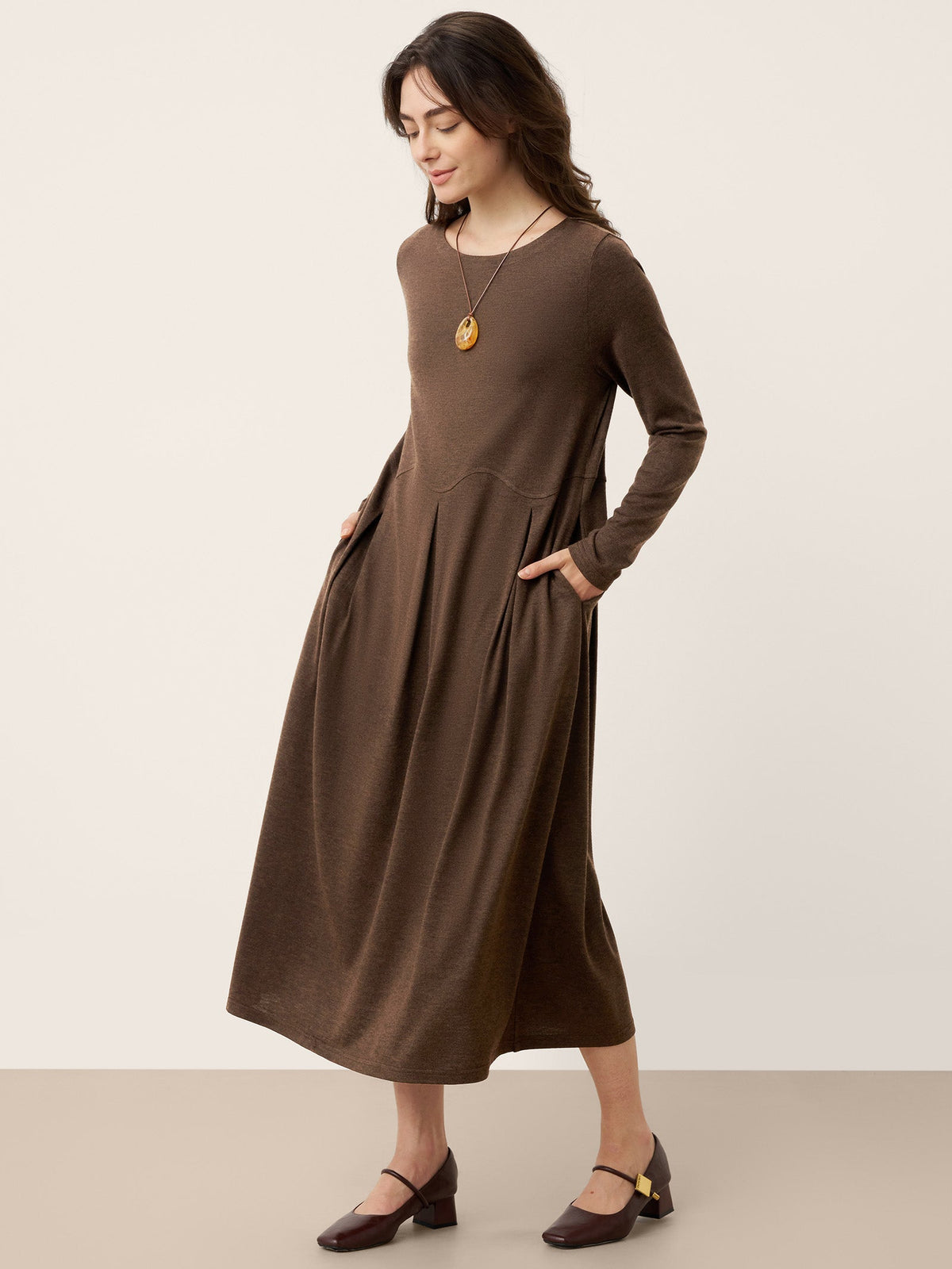 Brown wool midi dress with sculpted pleats and long sleeves; skirt flares at seams.