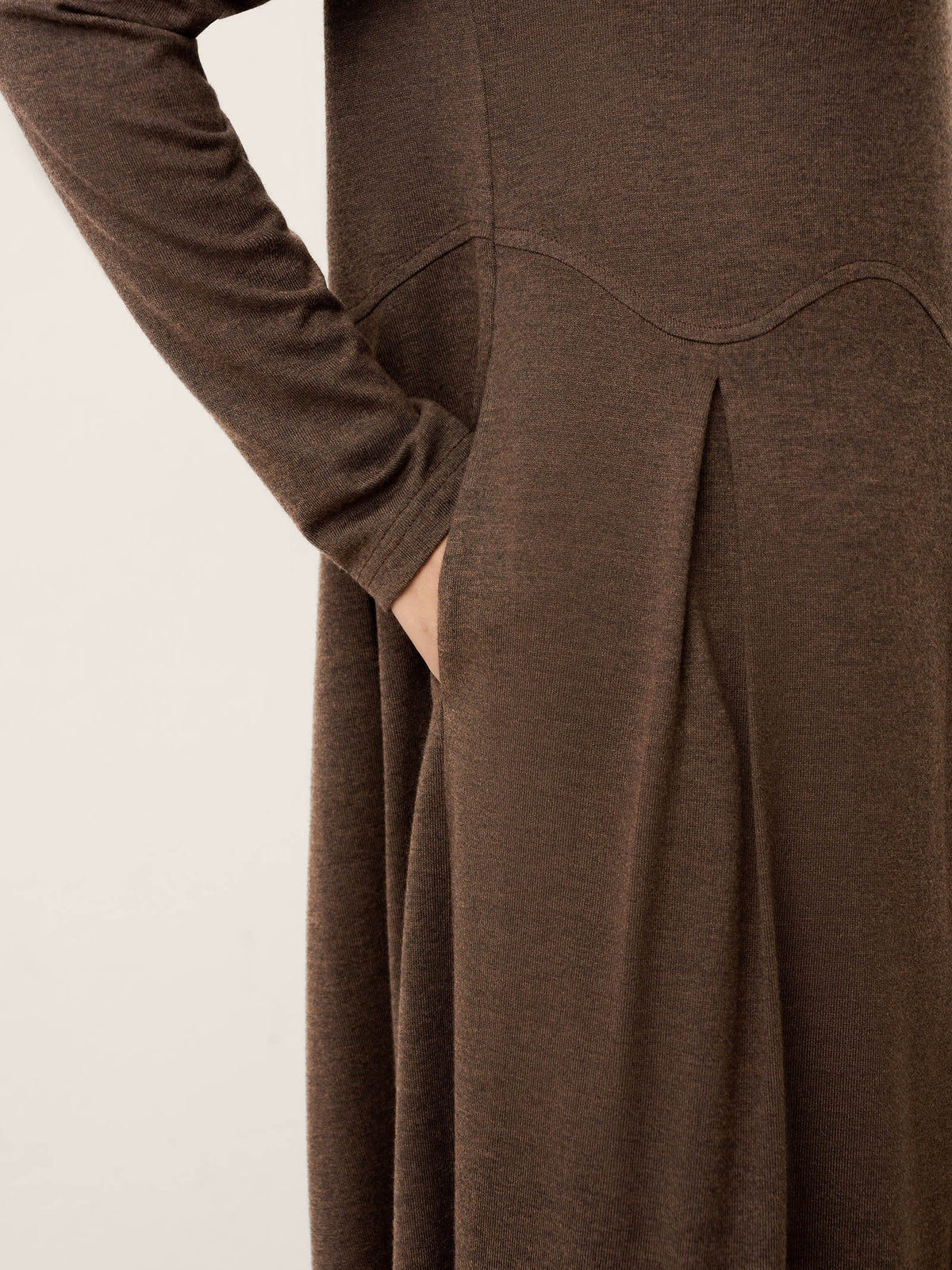 Close-up of brown pleated wool midi skirt with curved arc-panel seam lines.