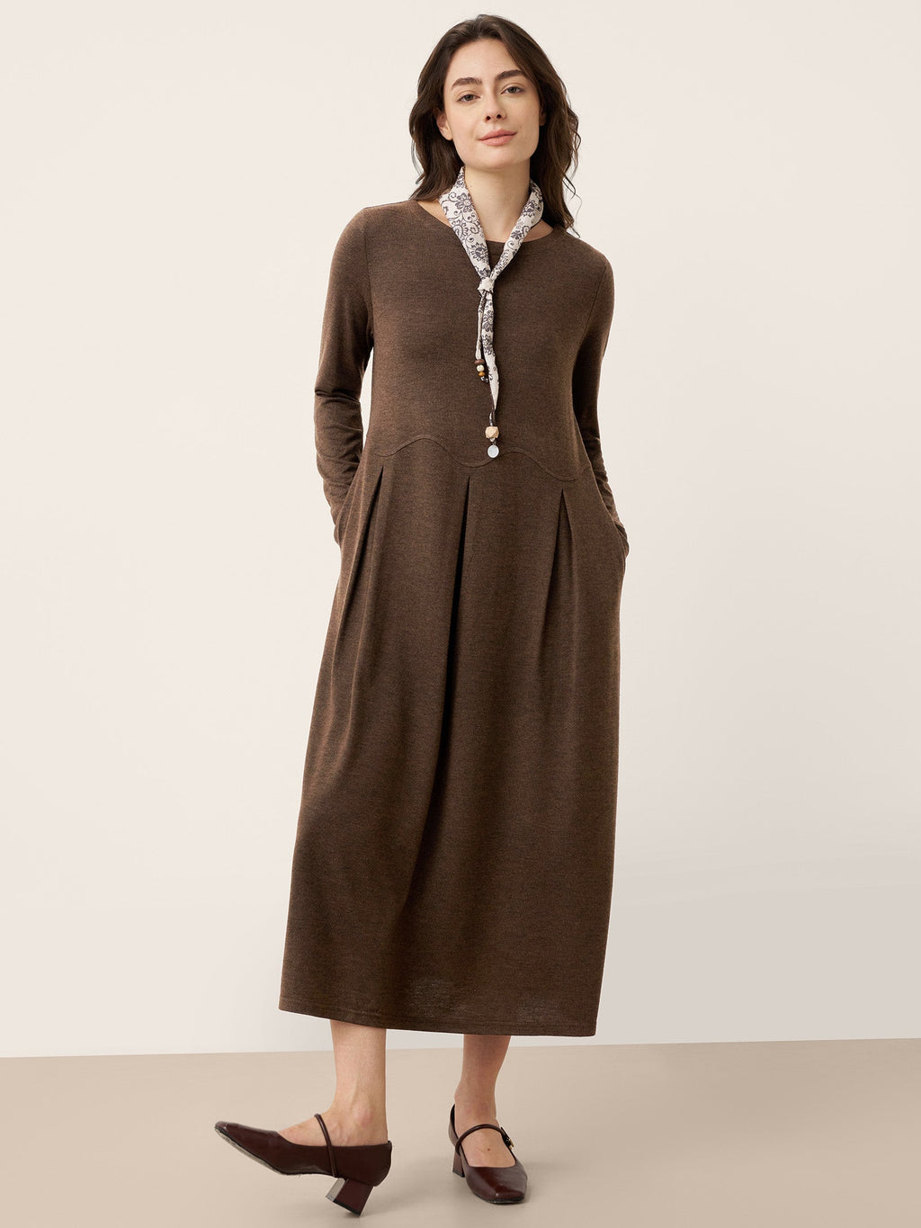 Brown wool midi dress with sculpted pleats, button front, and curved arc-panel seams.