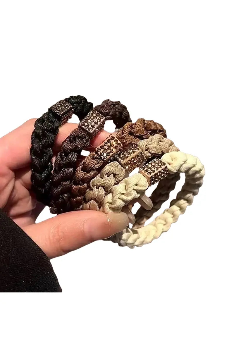 Assorted braided hair ties in black, brown, tan, and cream with jeweled cube centers.