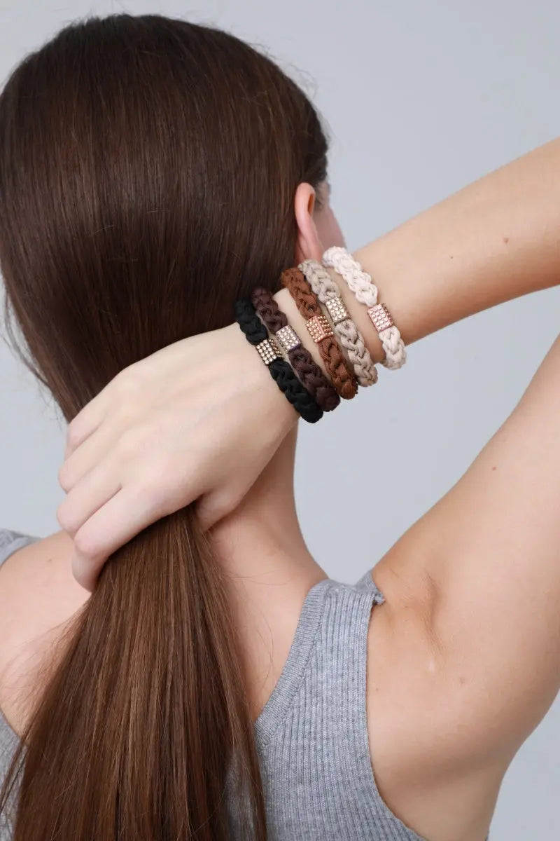 Braided hair ties worn on wrist: black, brown, and cream rings with jeweled center beads.