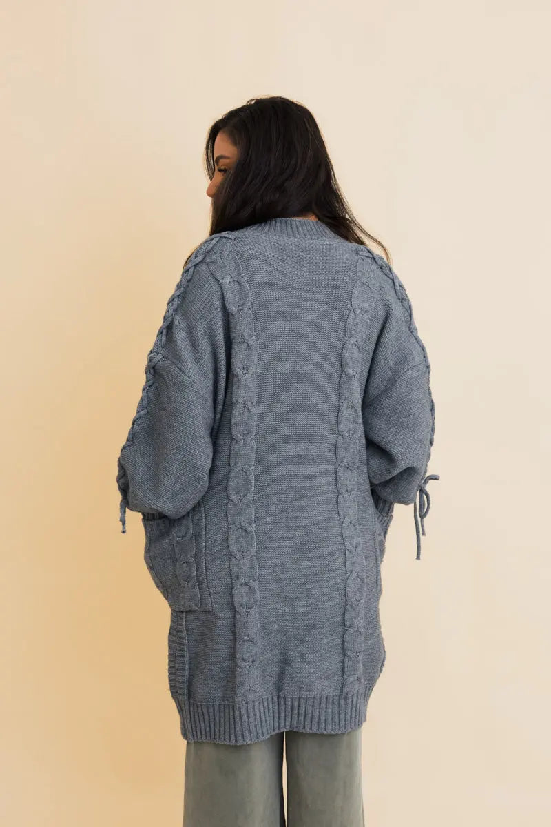 Blue cable-knit cardigan back view with tie sleeves and ribbed knit hem