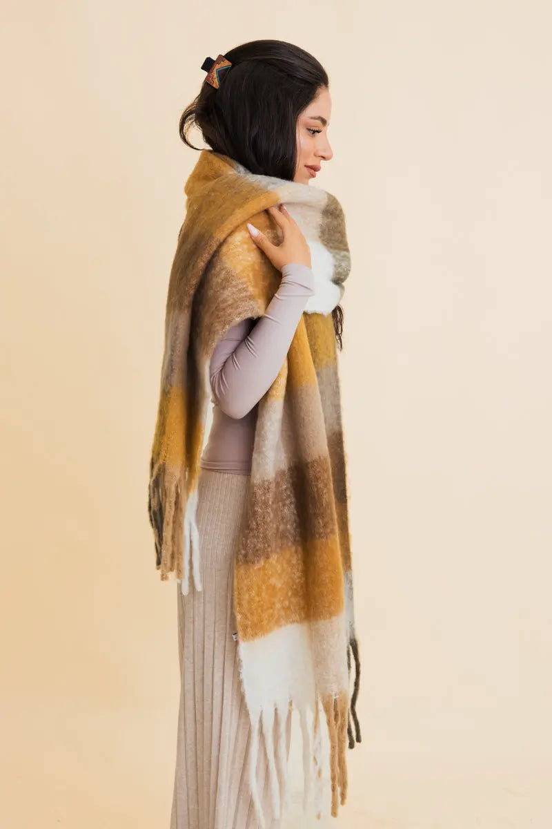 Oversized plaid fringe scarf draped on shoulder; olive, gold, gray, and white tassels