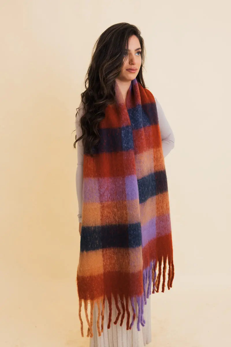 Oversized plaid scarf draped over shoulder in rust and blue with long fringe
