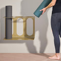Gold yoga mat rack holding three rolled yoga mats, with one mat lifted