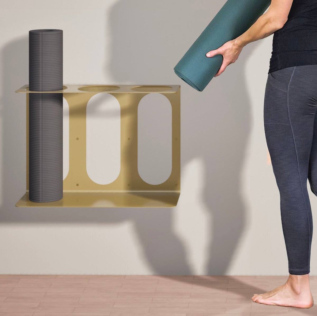 Gold yoga mat rack holding three rolled yoga mats, with one mat lifted