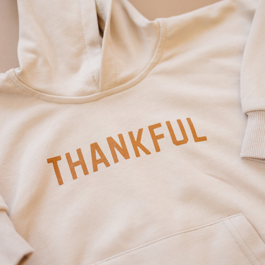 Close-up of hooded sweatshirt romper with 'THANKFUL' orange text and front pocket seam