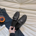 Black women's loafers with metal buckle and decorative F plate, flat low heel.