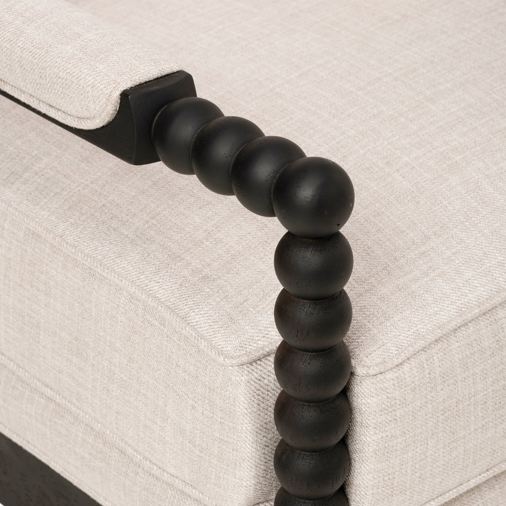 Upholstered accent chair close-up of the dark wood bead-style armrest and beige fabric cushions