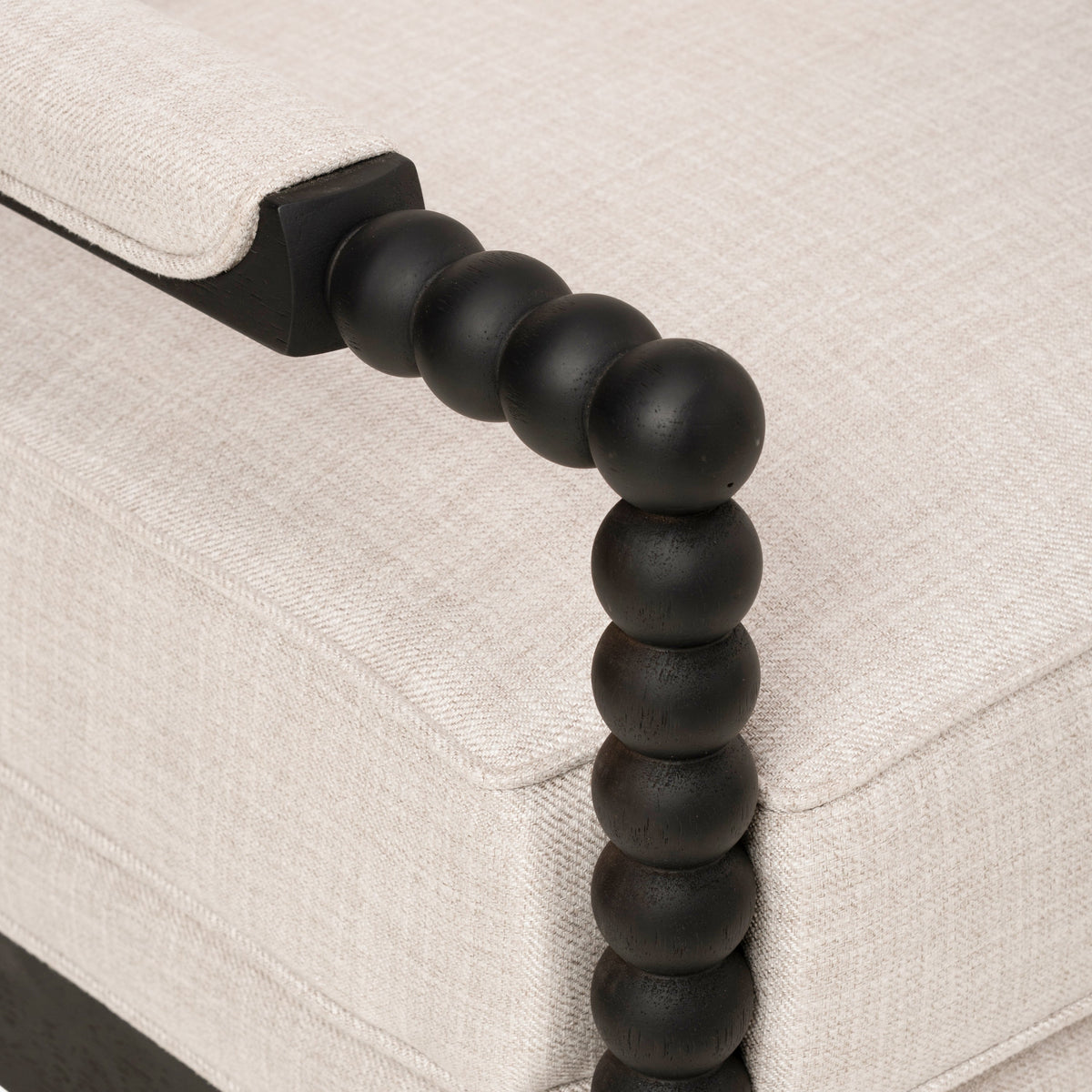 Upholstered accent chair close-up of the dark wood bead-style armrest and beige fabric cushions