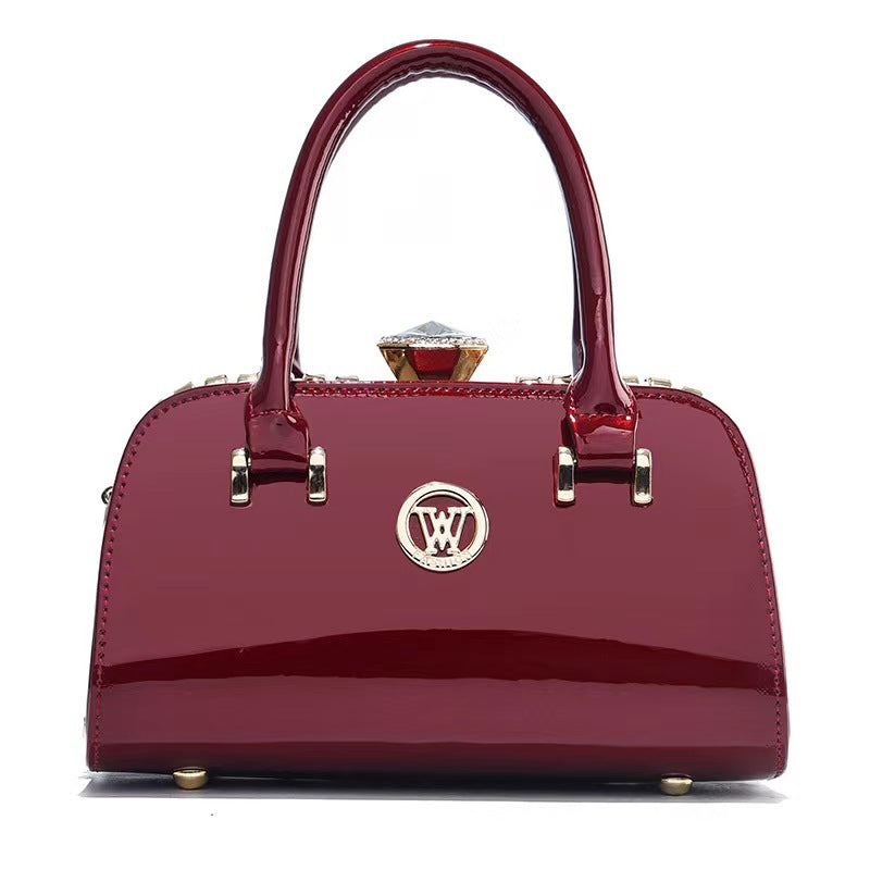 Wine red patent leather handbag with front logo, top handles, and diamond clasp