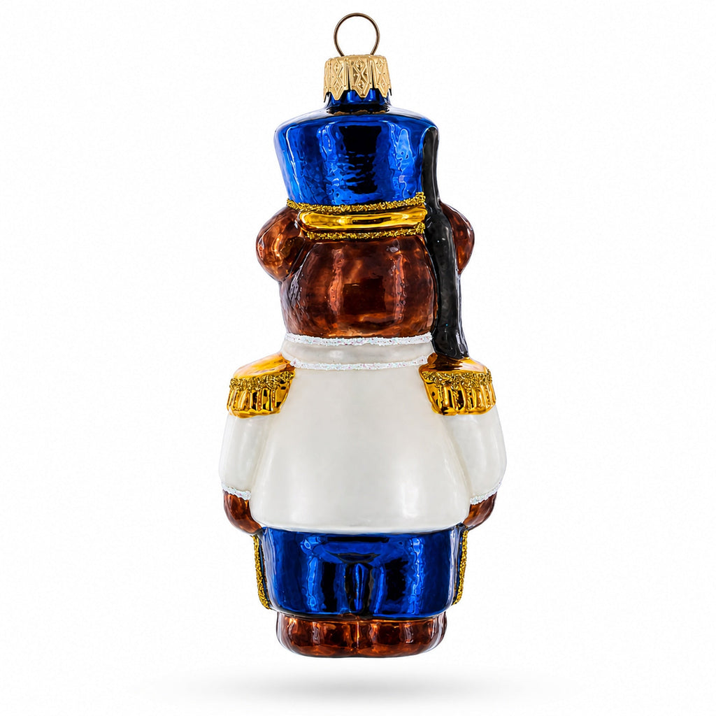 Glass nutcracker bear ornament front view, blue hat, brown body, white coat and gold trim