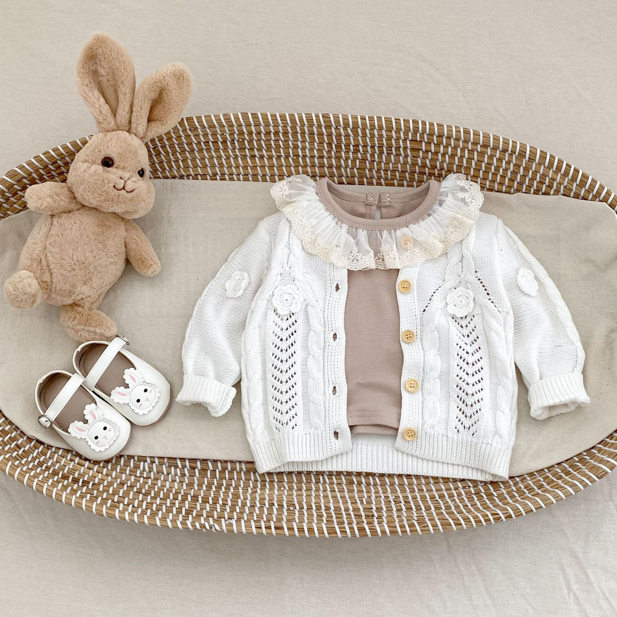 Cream hand-knit baby jacket with ruffled shoulders, flower motifs, button front