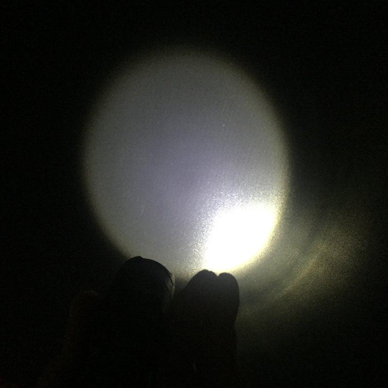 Mini handheld LED flashlight projecting a bright white beam from the front lens